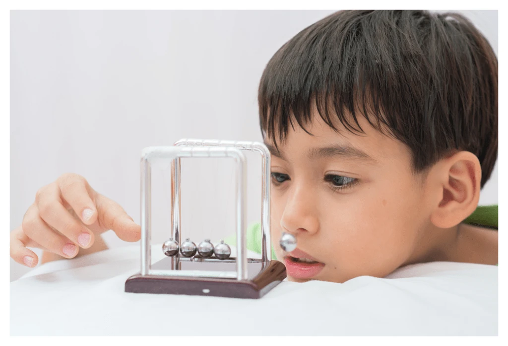 Young boy concentrating on a Newtons cradle during a hypnotherapy session.