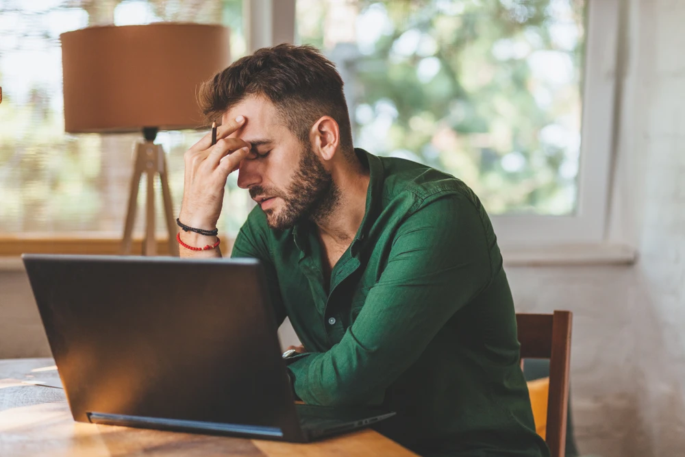 Stressed young man sitting in front of laptop, holding his head