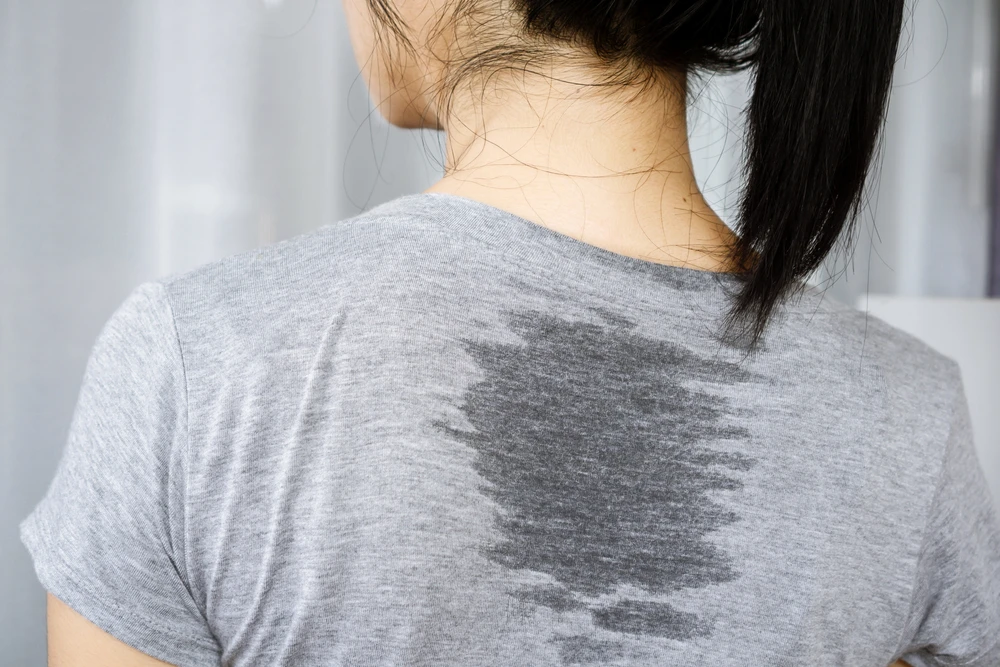 Women in grey cotton t-shirt with dark sweat mark between her shoulder blades. Sweat is a common trigger for eczema flare-up